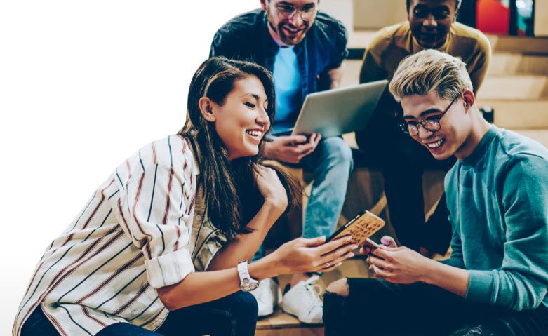 Nelnet Campus Commerce New Website - A group of smiling students sit gathered around phones and laptops sharing experiences.