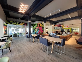 Interior view of The Green Squirrel café at Nelnet Center, showing tables, chairs, a café counter, colorful mural graphics, and a high ceiling with decorative architectural details.