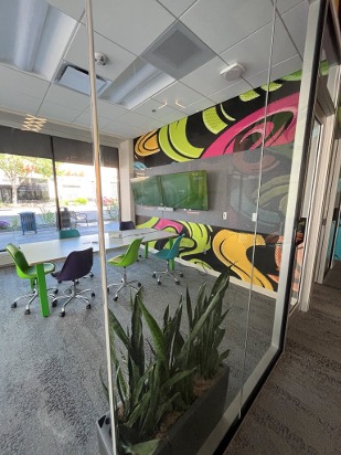 Glass-walled conference room inside The Green Squirrel at Nelnet Center, with colorful mural graphics, collaborative seating, and natural light from street-facing windows.
